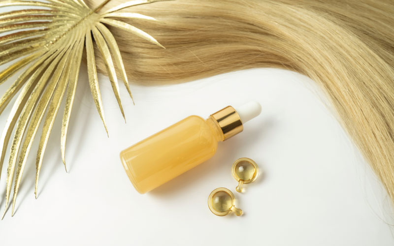 imagem de uma mecha de cabelo louro ao lado de uma garrafa de óleo capilar, simbolizando uma das formas de tratar cabelo quebradiço